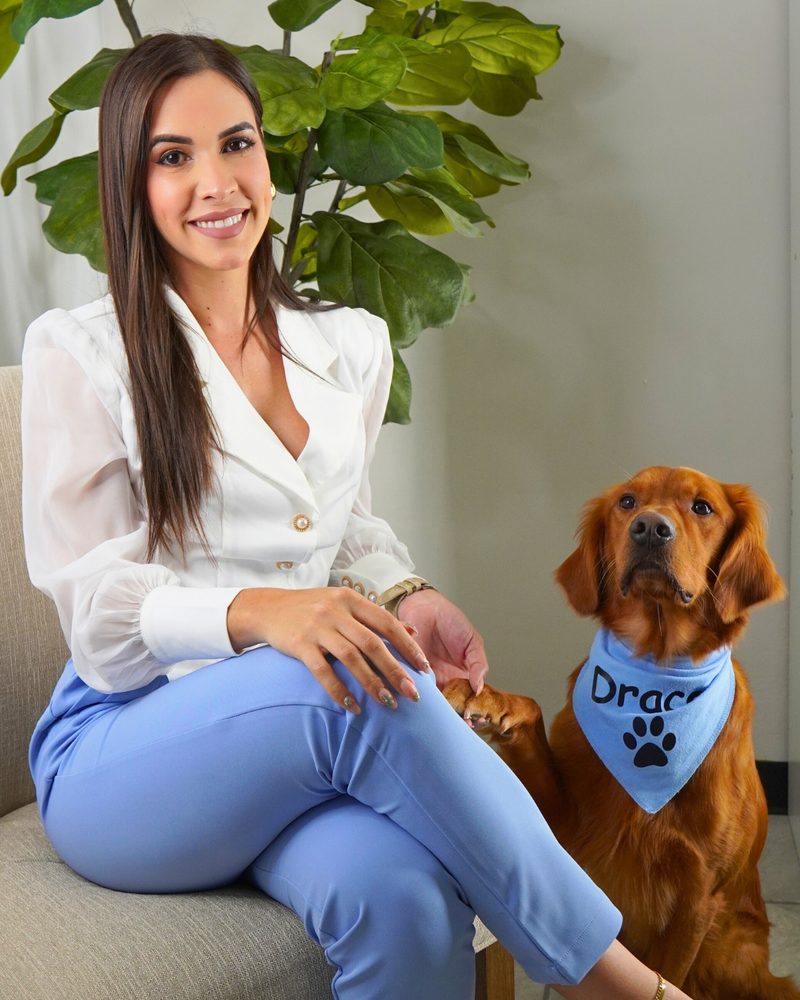 La psicóloga Jaidelys Acevedo sentada junto a Draco, golden retriever con pañuelo azul con su nombre